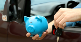 Mann im Auto mit Schlüssel und Sparschwein